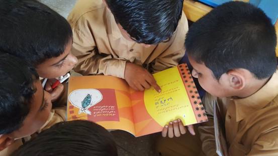 Four children looking down at a book, with one using his finger to point at the words in arabic.
